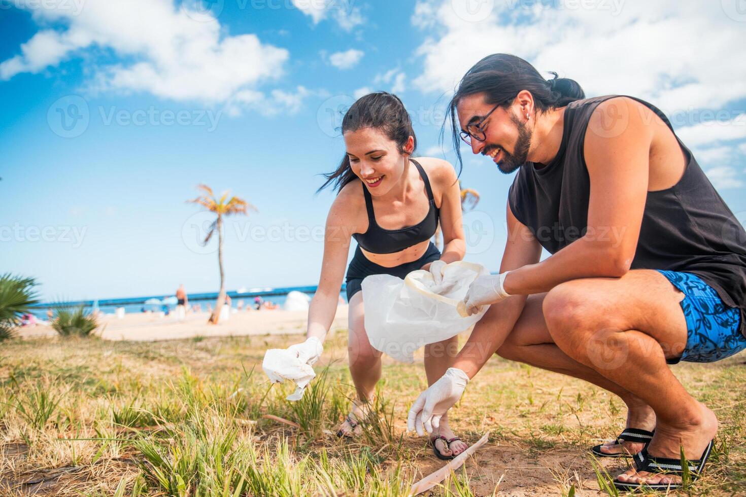 A man and a woman are picking up trash on a beach. They are both wearing gloves photo