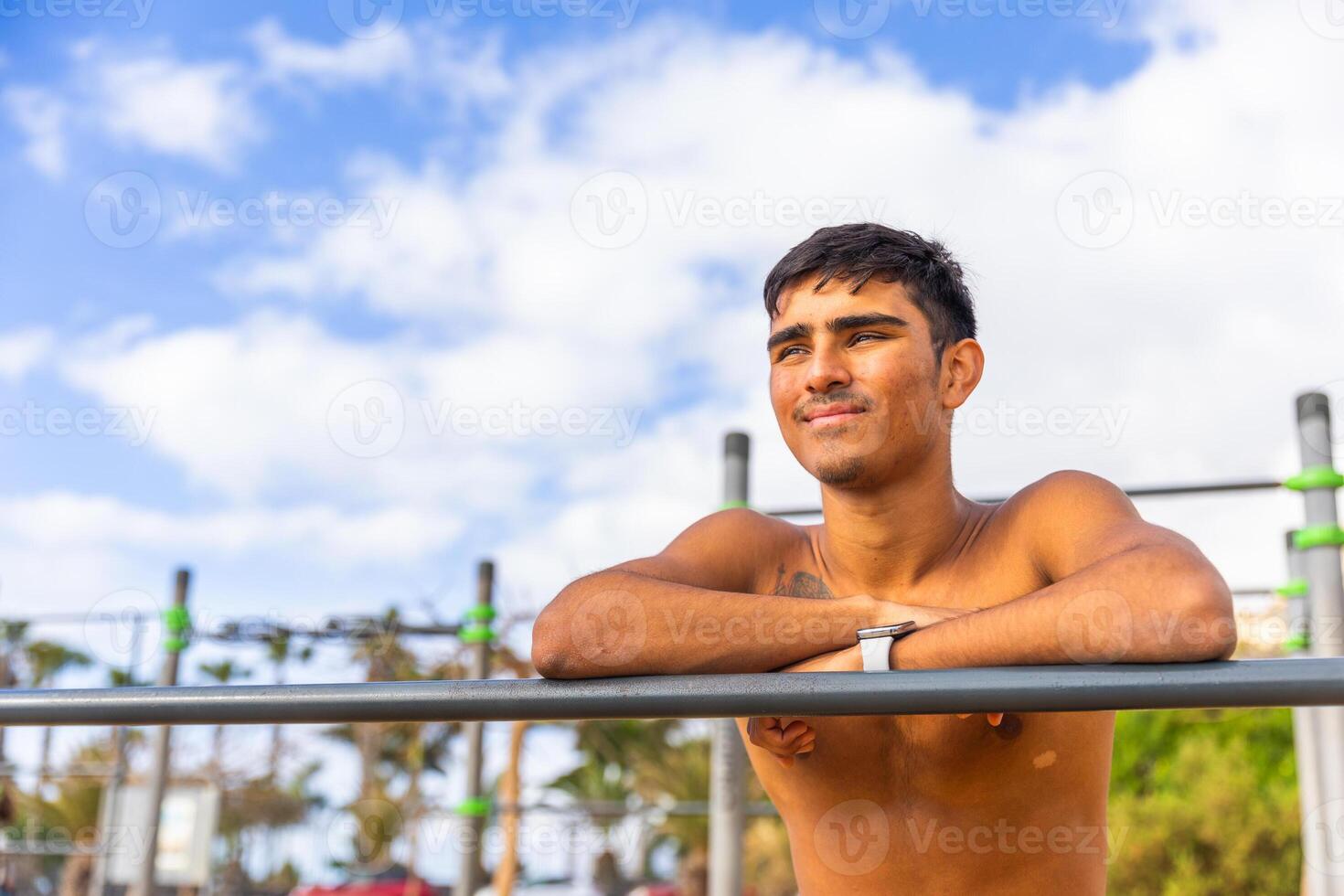 A man is standing on a metal bar with his arms crossed, sportsman at the outdoor gym photo