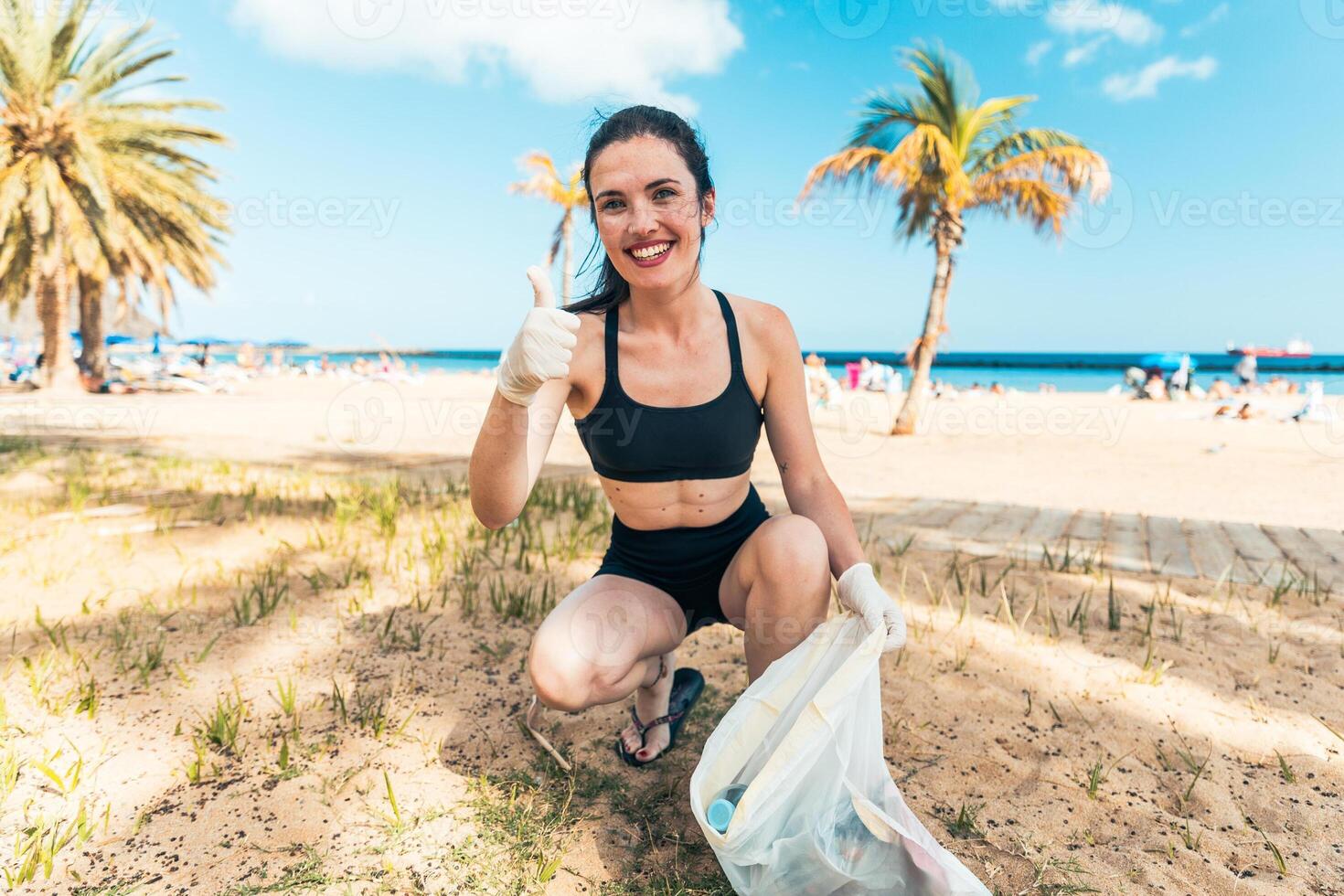 A woman is kneeling on the beach, showing the thumbs up and collecting photo