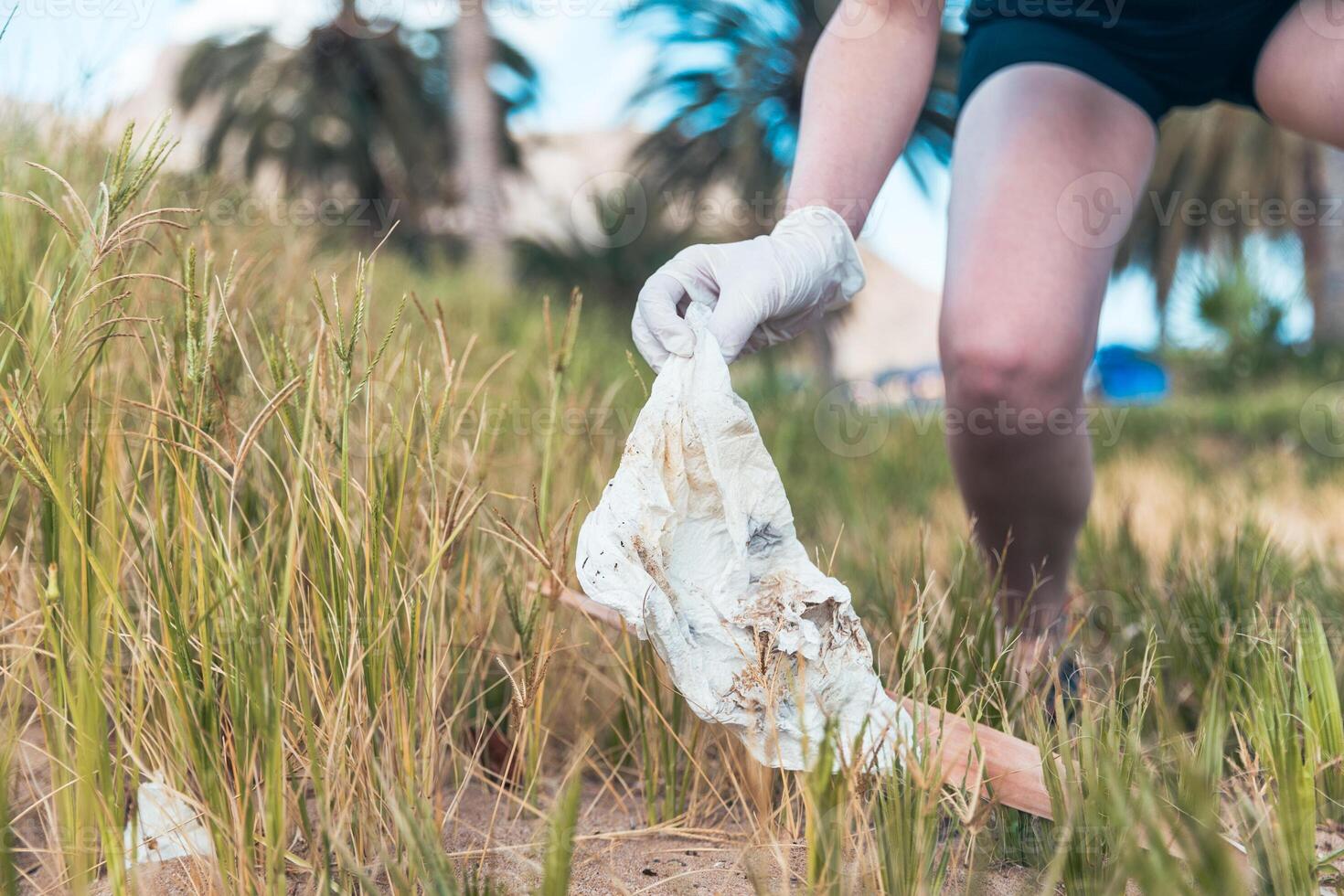 A person is picking up trash at the beach, The person is wearing gloves and is holding a piece of trash. photo