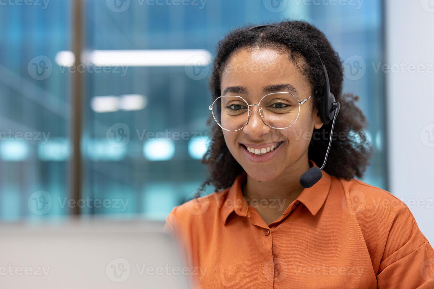 A professional woman wearing a headset and glasses works in a corporate setting. She is smiling confidently while engaging in communication, showcasing a positive attitude. photo