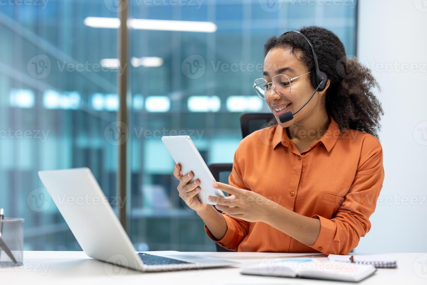 Woman with headset and tablet computer working inside office with laptop, support and helpline worker. photo
