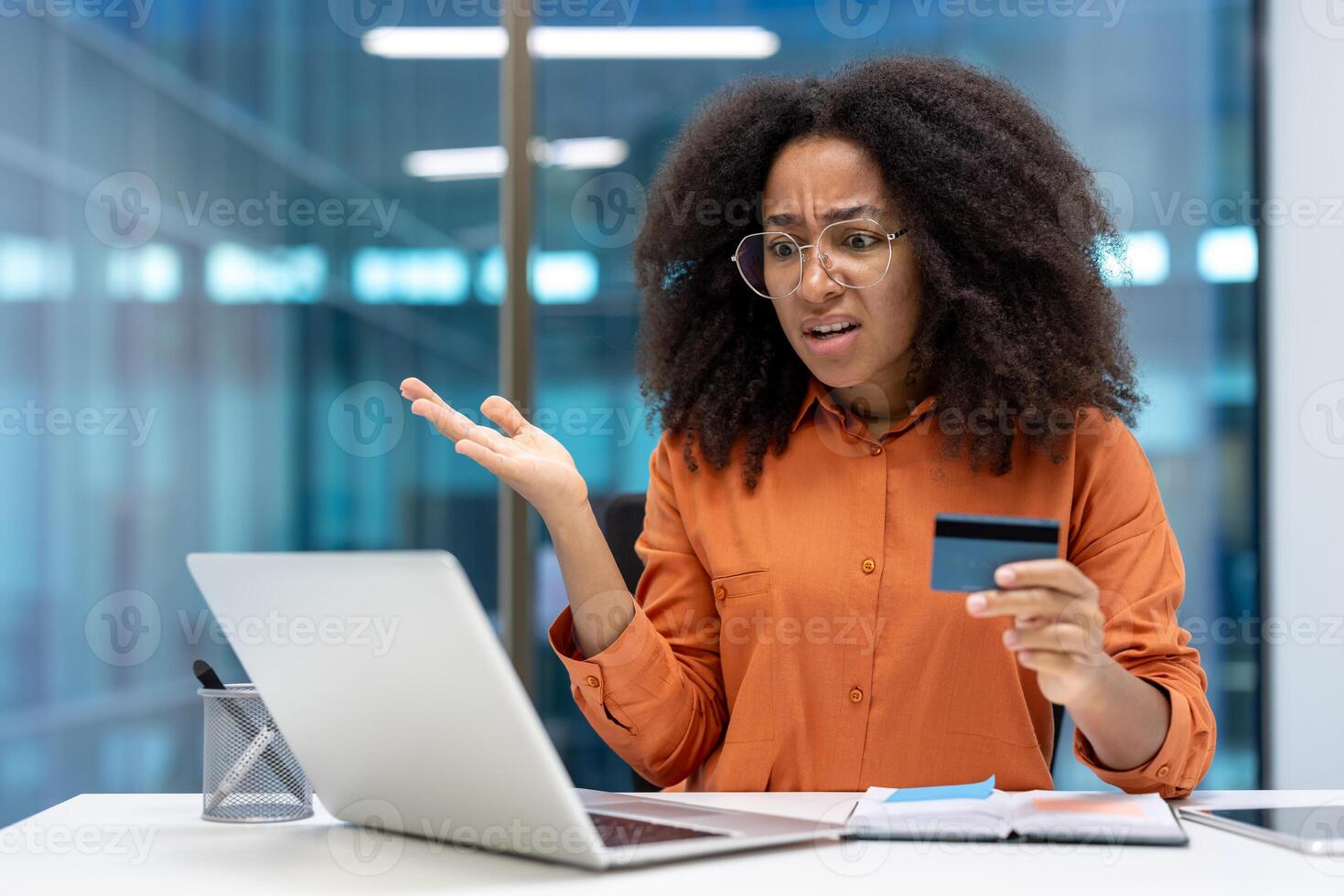 Confused woman holding credit card while using laptop in office. Frustrated expression suggests problem with online shopping or payment issues, creating concern and dissatisfaction. photo