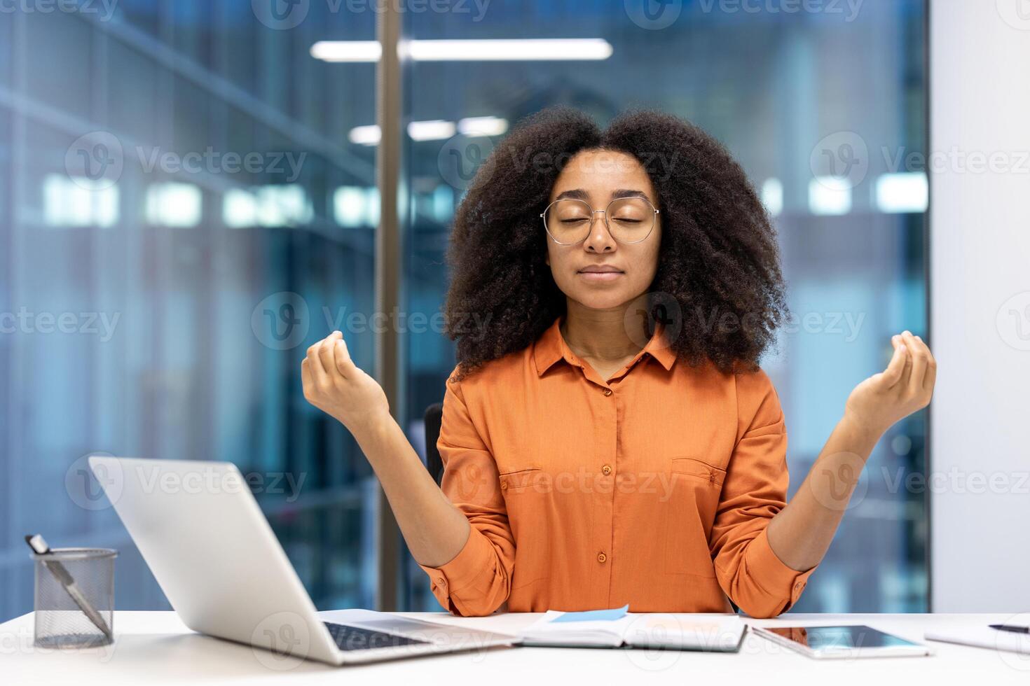 Relaxed woman meditating at office desk in front of laptop. Practicing mindfulness and finding inner peace amidst work. Emphasizing calmness, relaxation, and mental wellness. photo