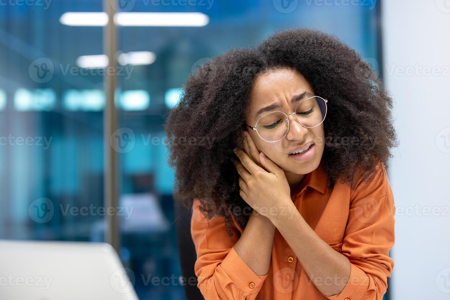 A young woman holds hand to ear, showcasing discomfort and ear pain, sitting at office. Her expression and gesture convey a sense of unease, possibly due to medical issues inflammation or otitis photo
