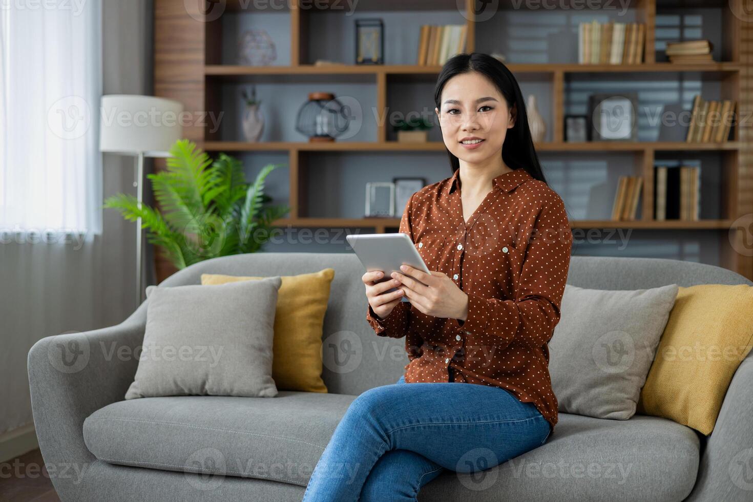 Portrait of young Asian woman, student smiling and looking at camera holding tablet computer, studying remotely sitting at home on sofa in living room, using online app. photo