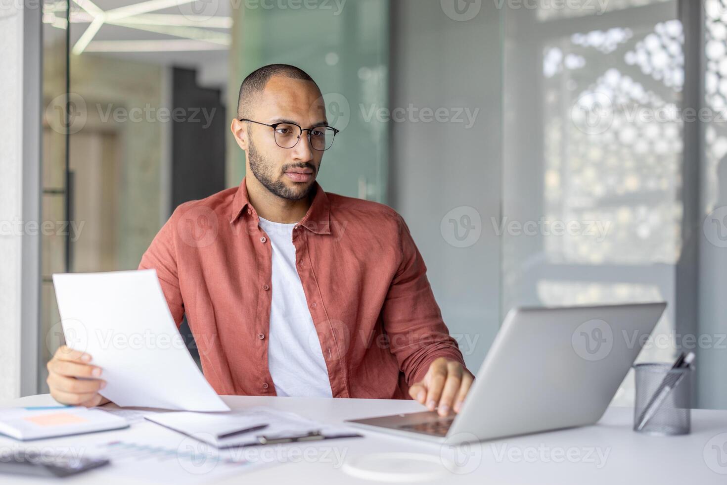 Serious focused businessman doing paperwork inside office, man in casual shirt working with documents contracts and reports, successful financier investor. photo