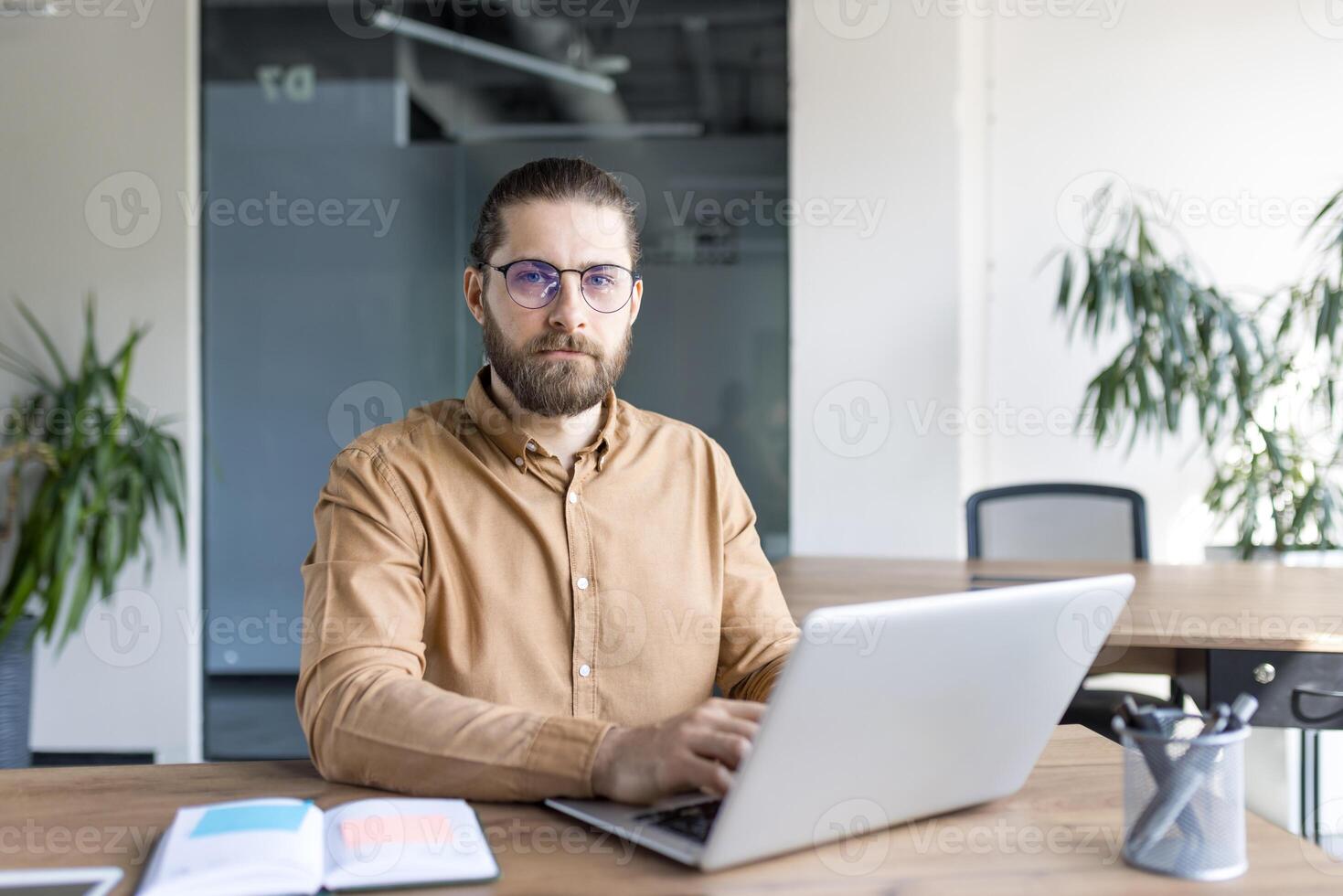 A focused professional at a desk working on a laptop, surrounded by office supplies and plants. Perfect image for business, technology, and office-related themes for presentations or advertisements. photo