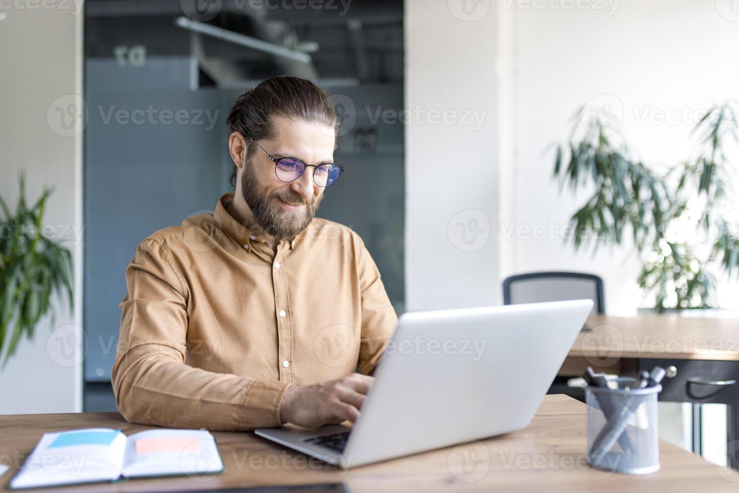 A male professional works confidently on a laptop at a wooden desk in a stylish office, focusing on business tasks with dedication. photo