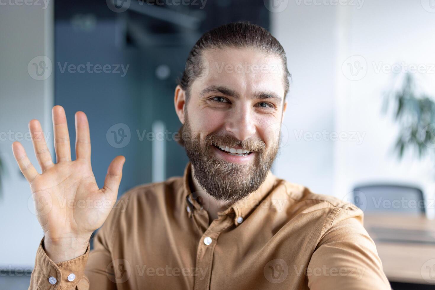 Friendly bearded professional making a warm gesture during a webcam meeting in a modern office setting. photo