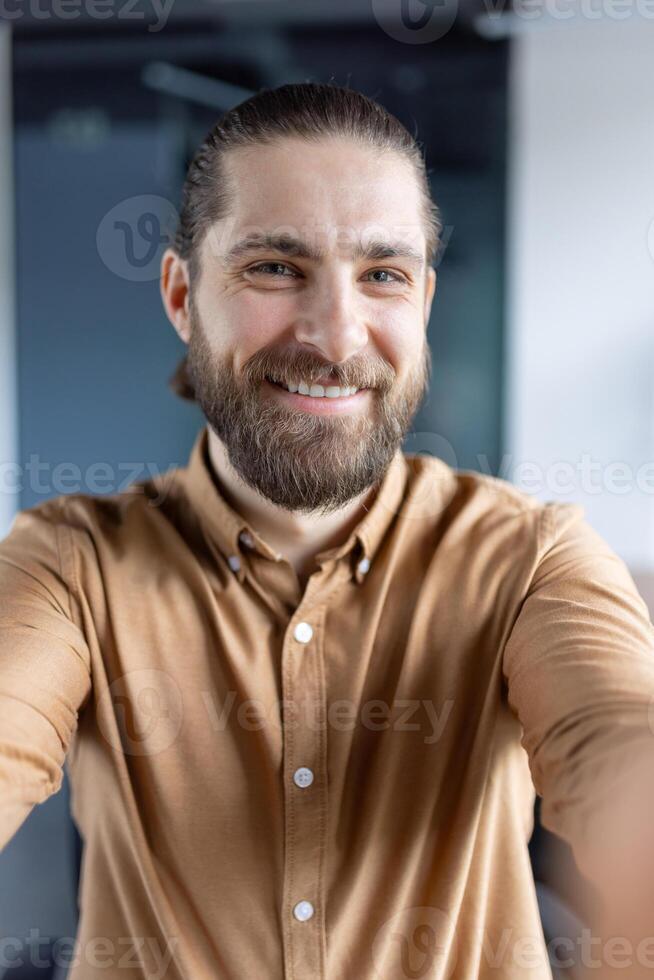 A cheerful individual in casual attire capturing a selfie in an office, emphasizing friendly and approachable professionalism. photo