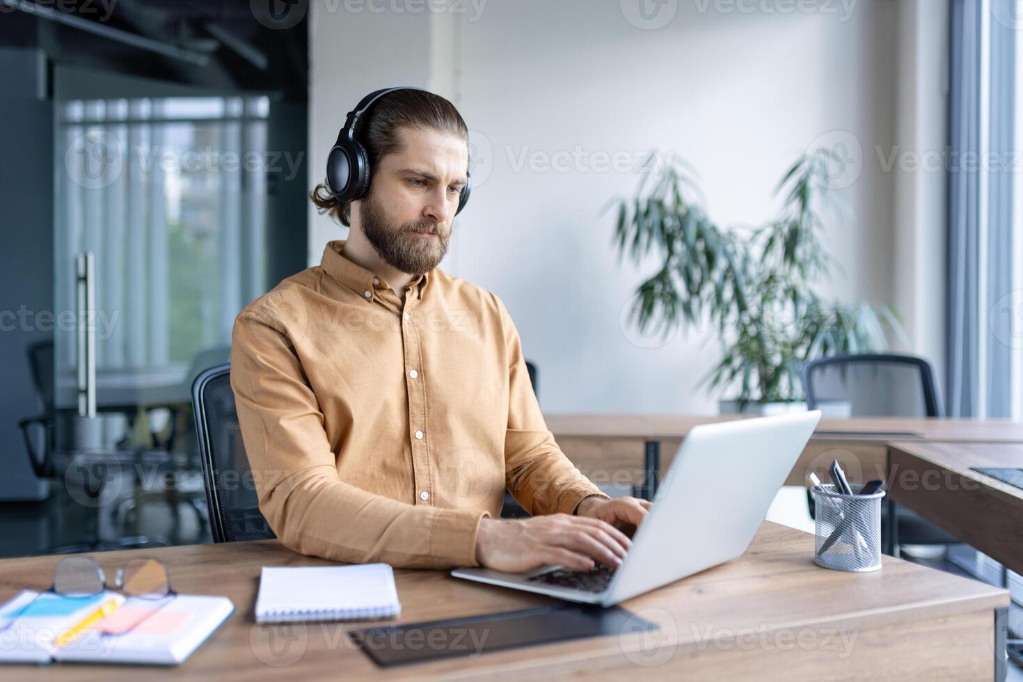 Focused business professional wearing headphones and working diligently on a laptop in an office. The image portrays concentration, productivity, and a professional work environment photo