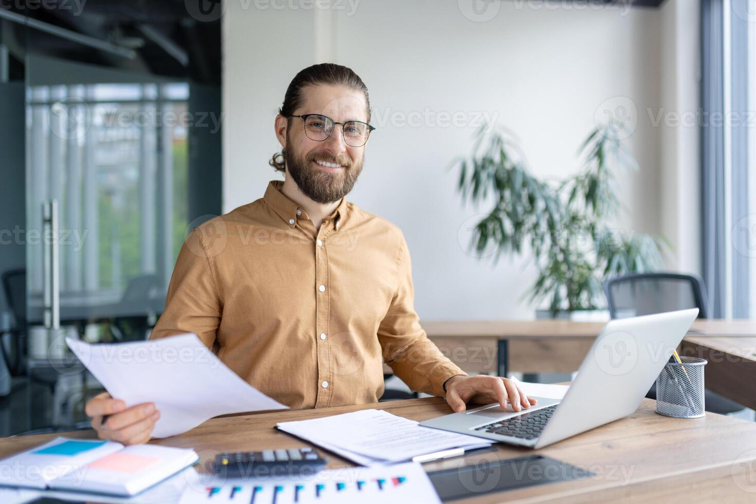 Smiling office worker sitting at desk with laptop, reviewing documents, and analyzing reports. The workspace exudes professionalism and productivity photo