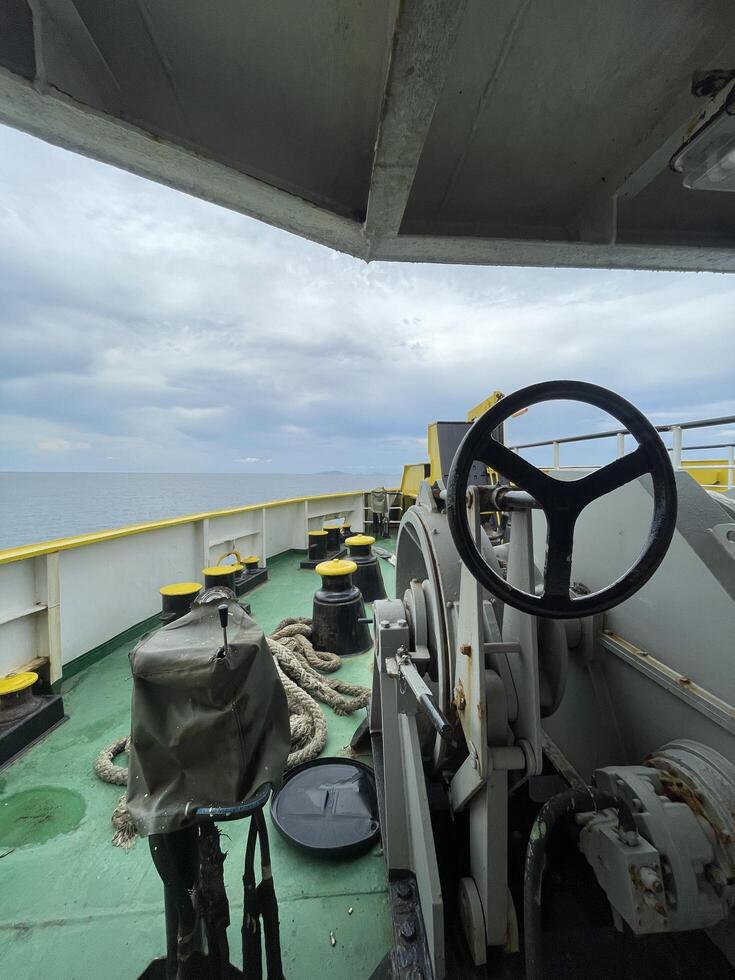 A ship's wheel frames a breathtaking seascape under a tranquil sky. Yellow deck fittings and a calm ocean create a peaceful, maritime scene photo