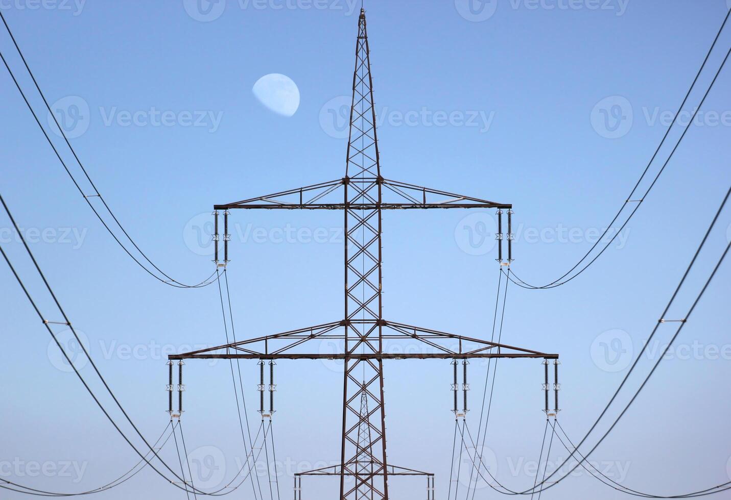 Symmetrical view on a high voltage power line. The moon is visible in the background. photo