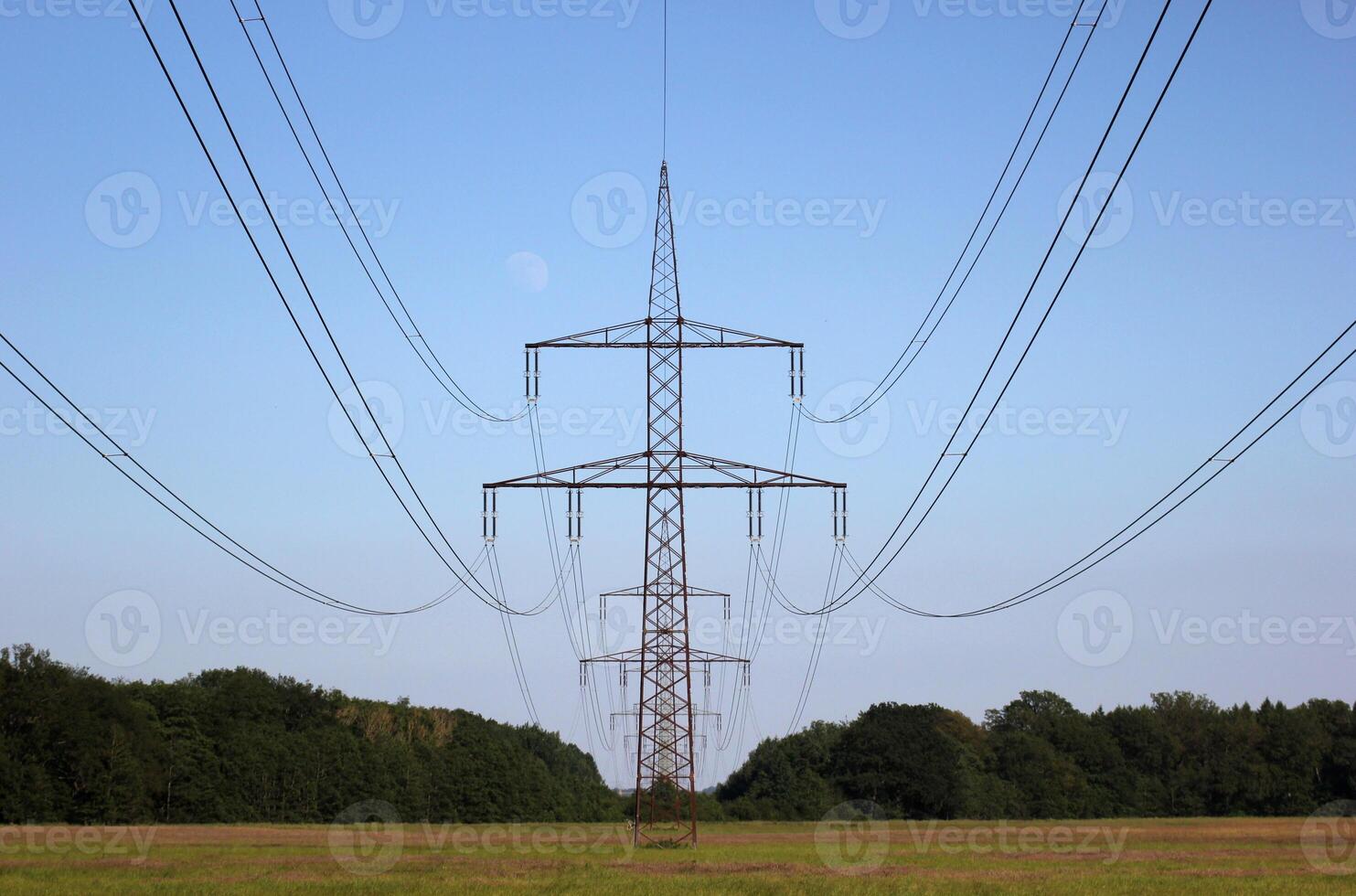 Symmetrical view on a high voltage power line on a rural landscape with forest to both sides. The moon is visible in the background. photo