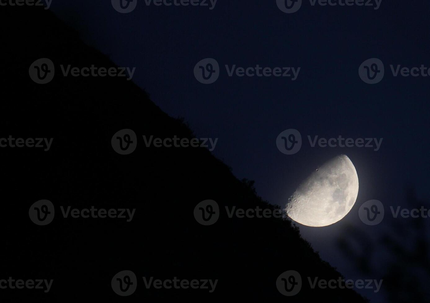 Partial moon on dark blue with slightly visible horizon in unusal angle. photo