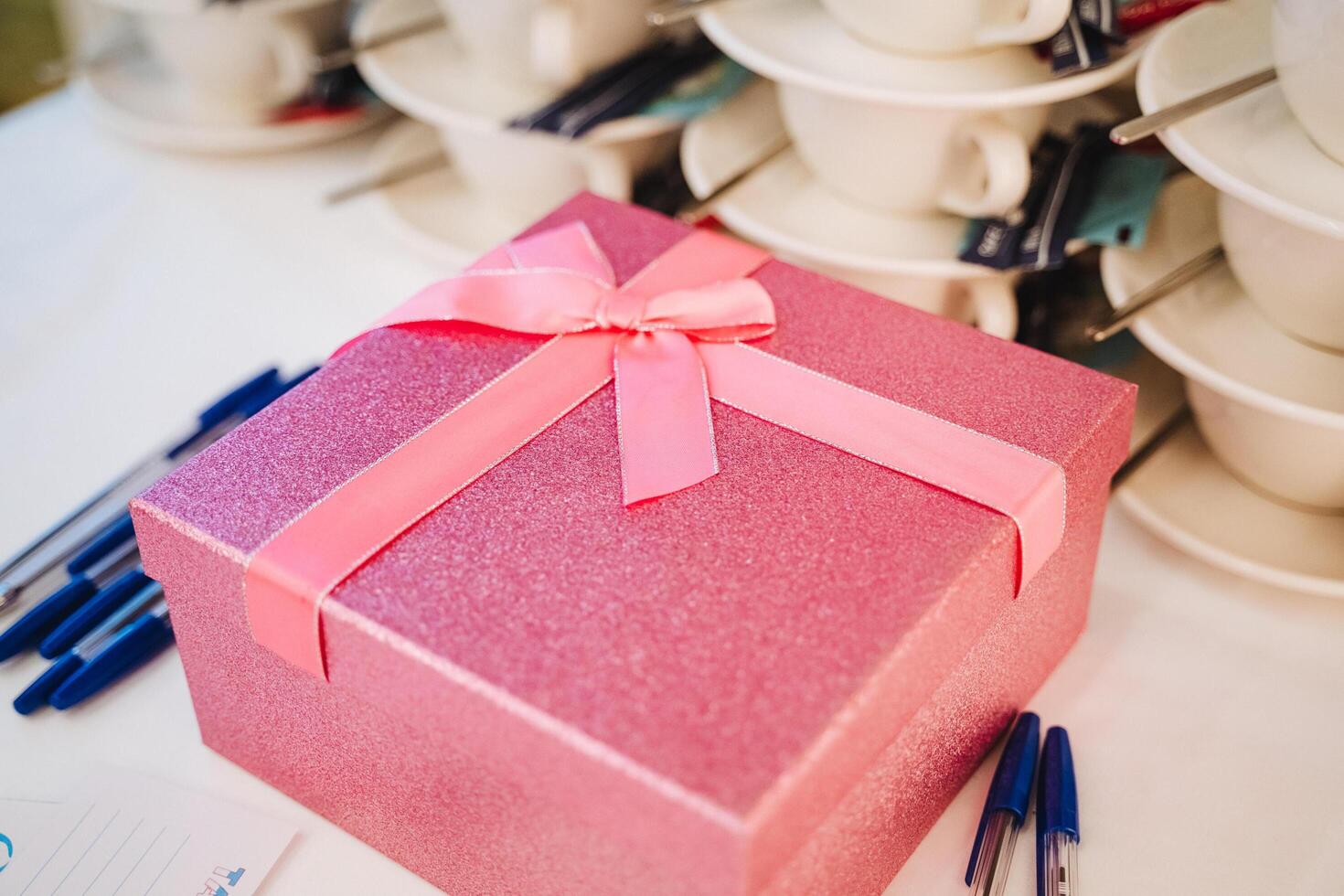 A charming pink gift box adorned with a stylish ribbon elegantly rests on a beautifully set table, creating an enchanting atmosphere that is ideal for any special occasion or celebration photo