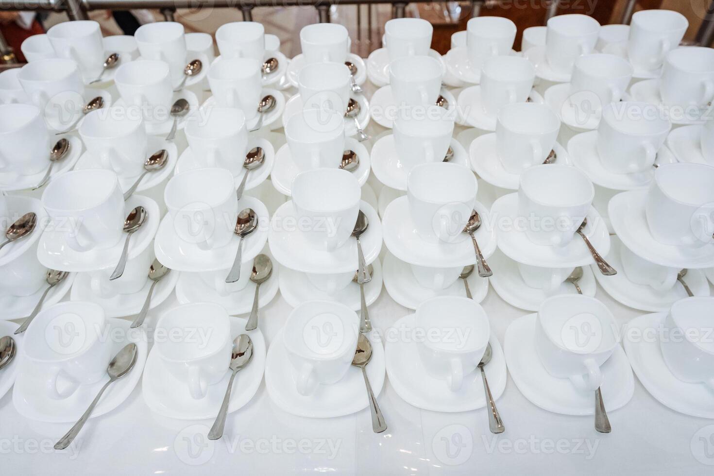 A row of elegant white cups with matching saucers and finely crafted spoons on a wellset table creates an inviting dining aesthetic, enticing guests to enjoy a delightful meal photo