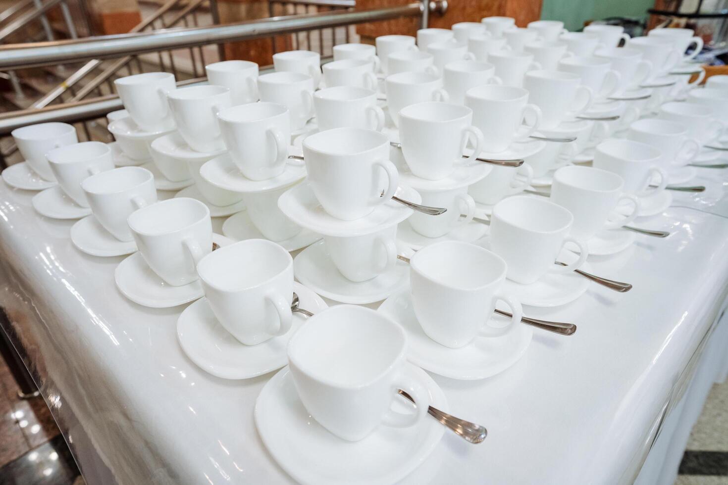 On the table, there is a neatly arranged row of white coffee cups sitting alongside their matching saucers, creating an inviting atmosphere for coffee lovers to enjoy a warm beverage photo