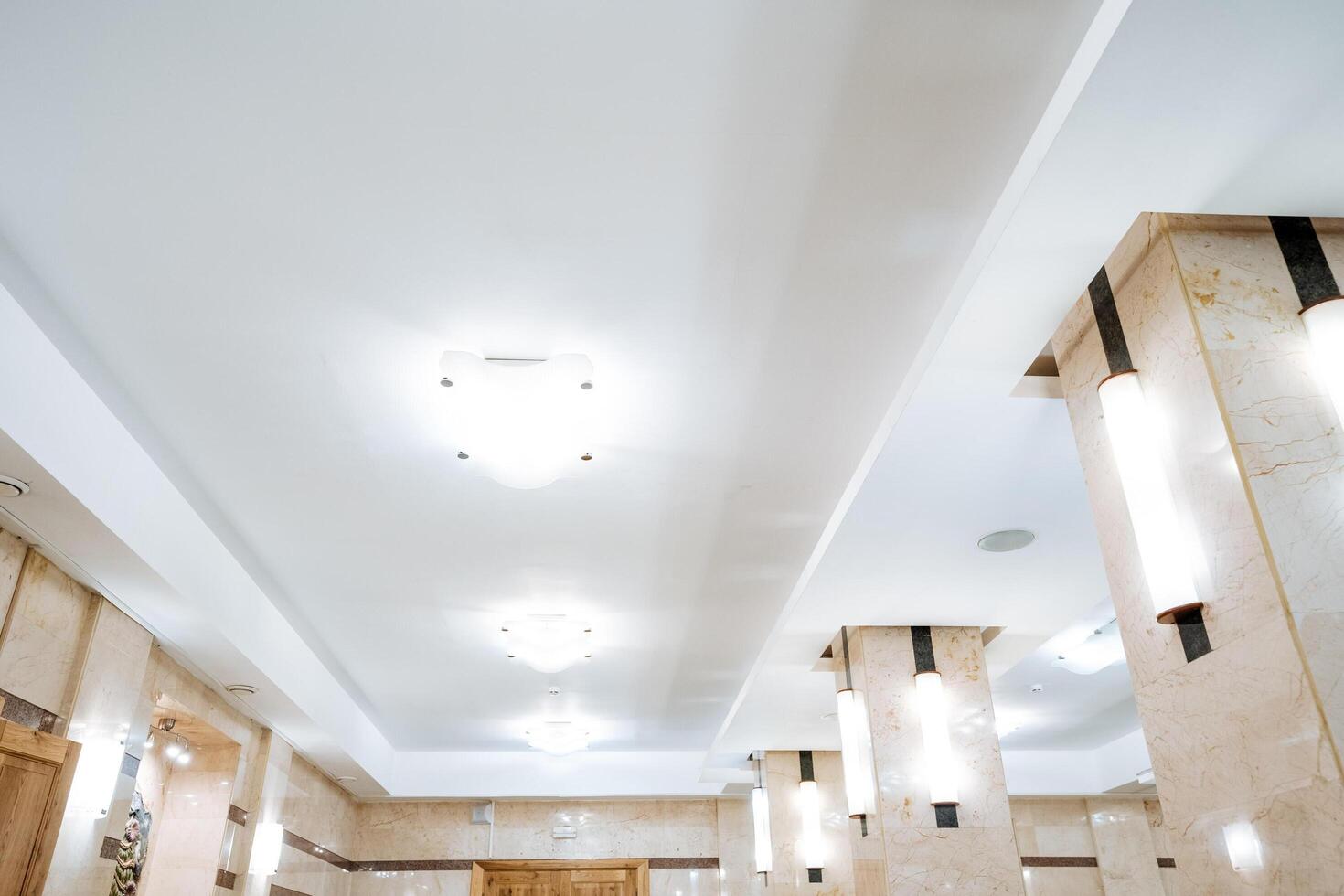 The spacious and welllit room boasts a pristine white ceiling and elegant columns, significantly enhancing its grandeur and creating a warm and inviting atmosphere for all who enter photo