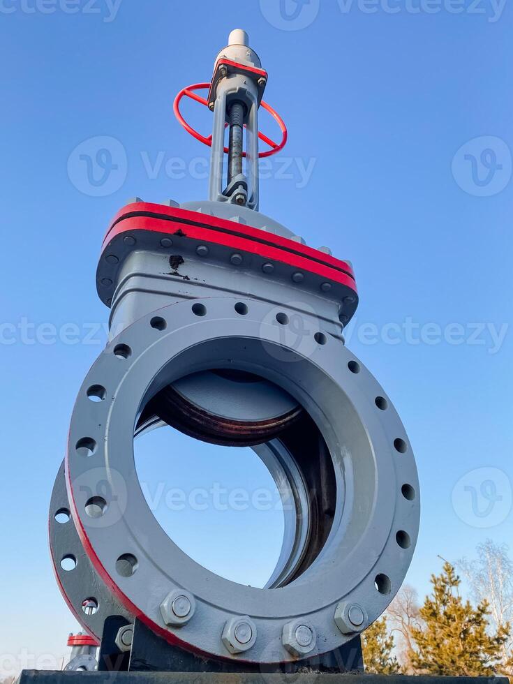 This image features a detailed closeup of a valve, with a beautiful blue sky serving as the backdrop, creating a striking contrast against the metallic structure of the valve photo