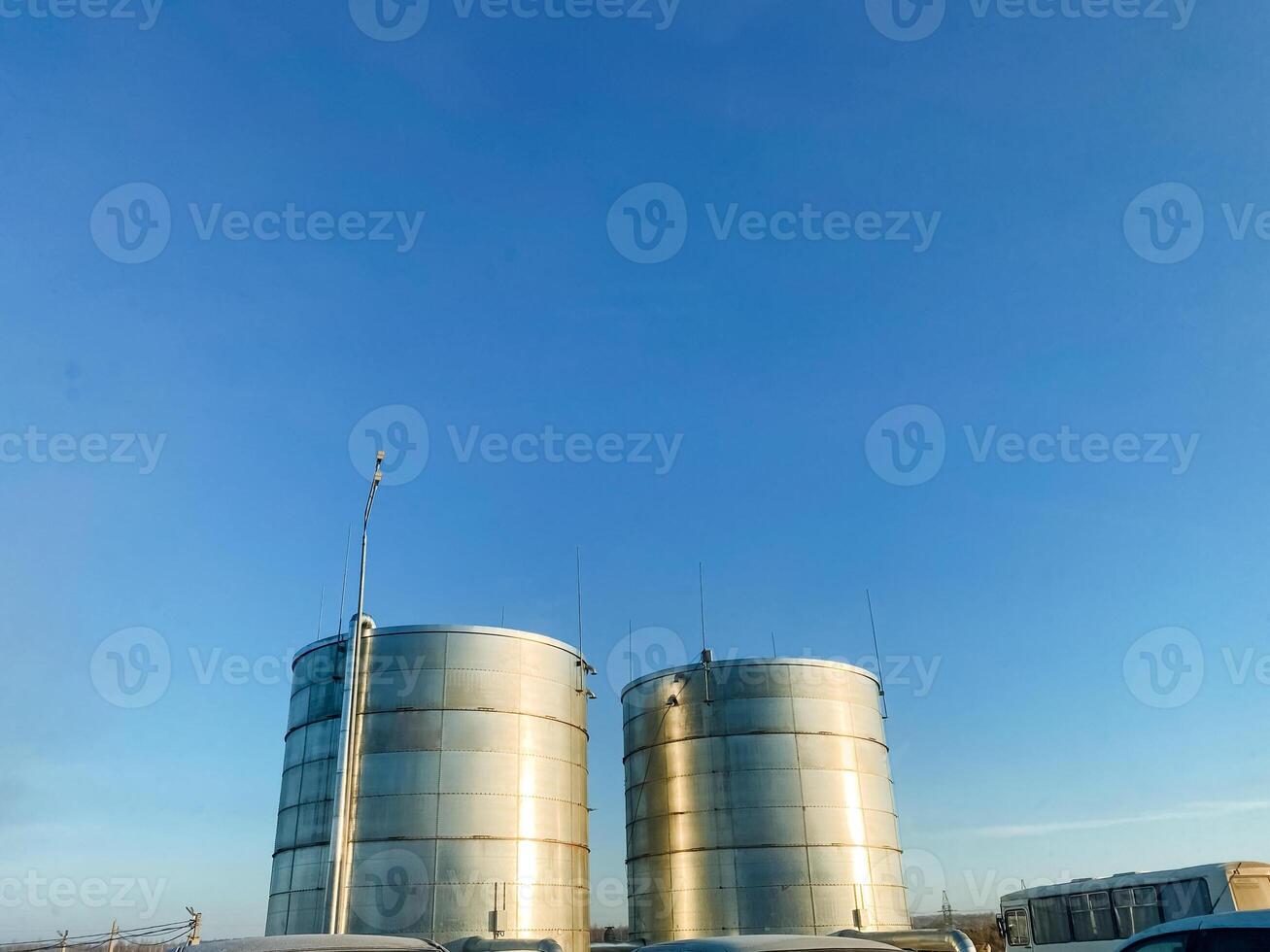 Two large, shiny stainless steel tanks stand tall against a vibrant blue sky, providing essential storage for various liquids, including gas, within an urban engineering landscape photo