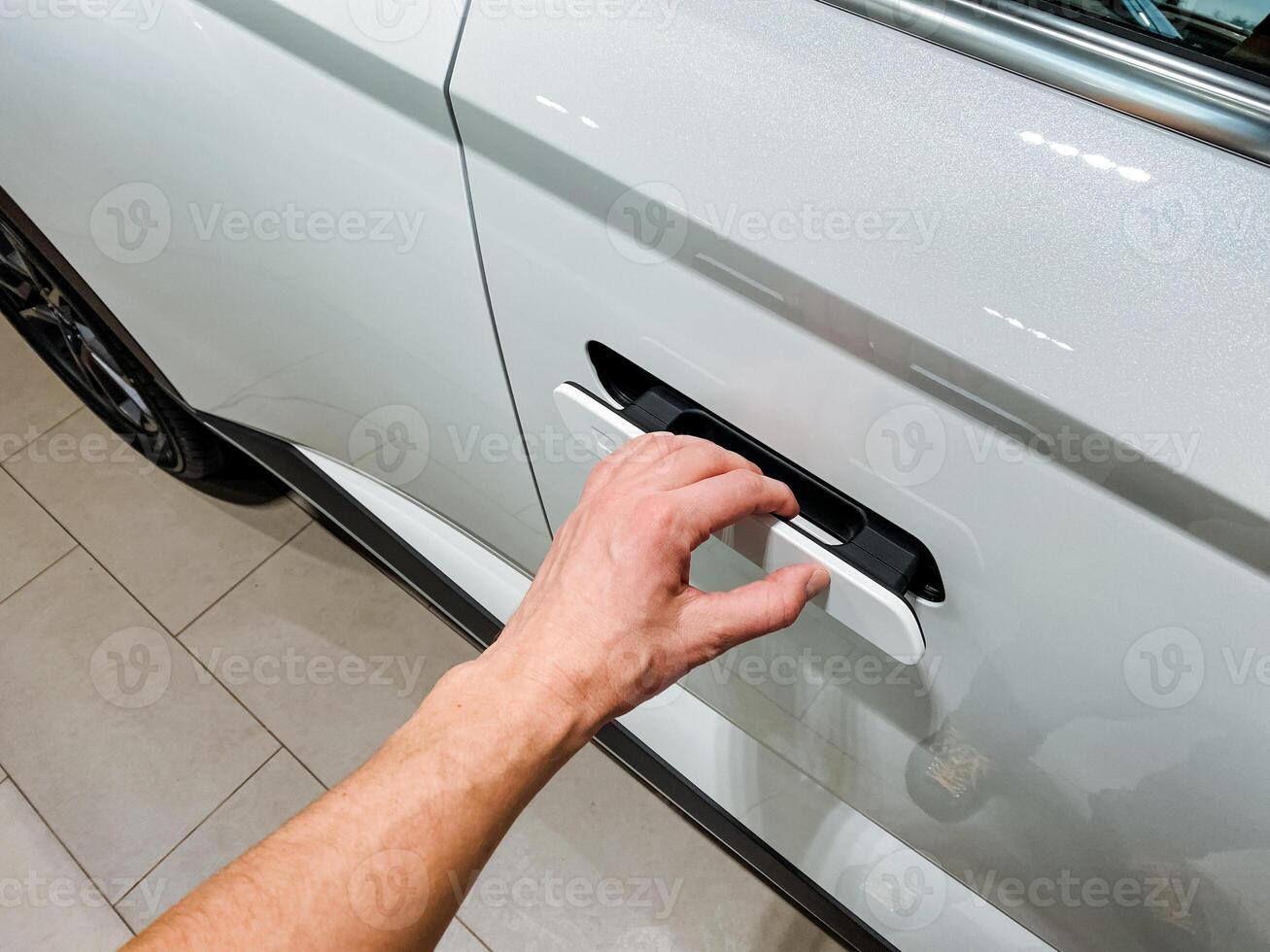 A person is currently in the process of successfully opening the door of a shiny and attractive silver car that is parked nearby, eager to get inside and begin their exciting journey photo