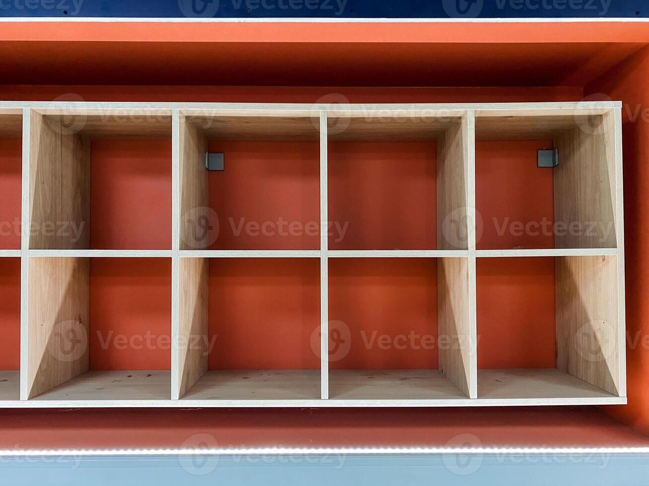 On a vibrant red wall, there is a wellcrafted wooden shelf that features dividers designed to organize items neatly and efficiently, enhancing the aesthetic appeal of the space photo
