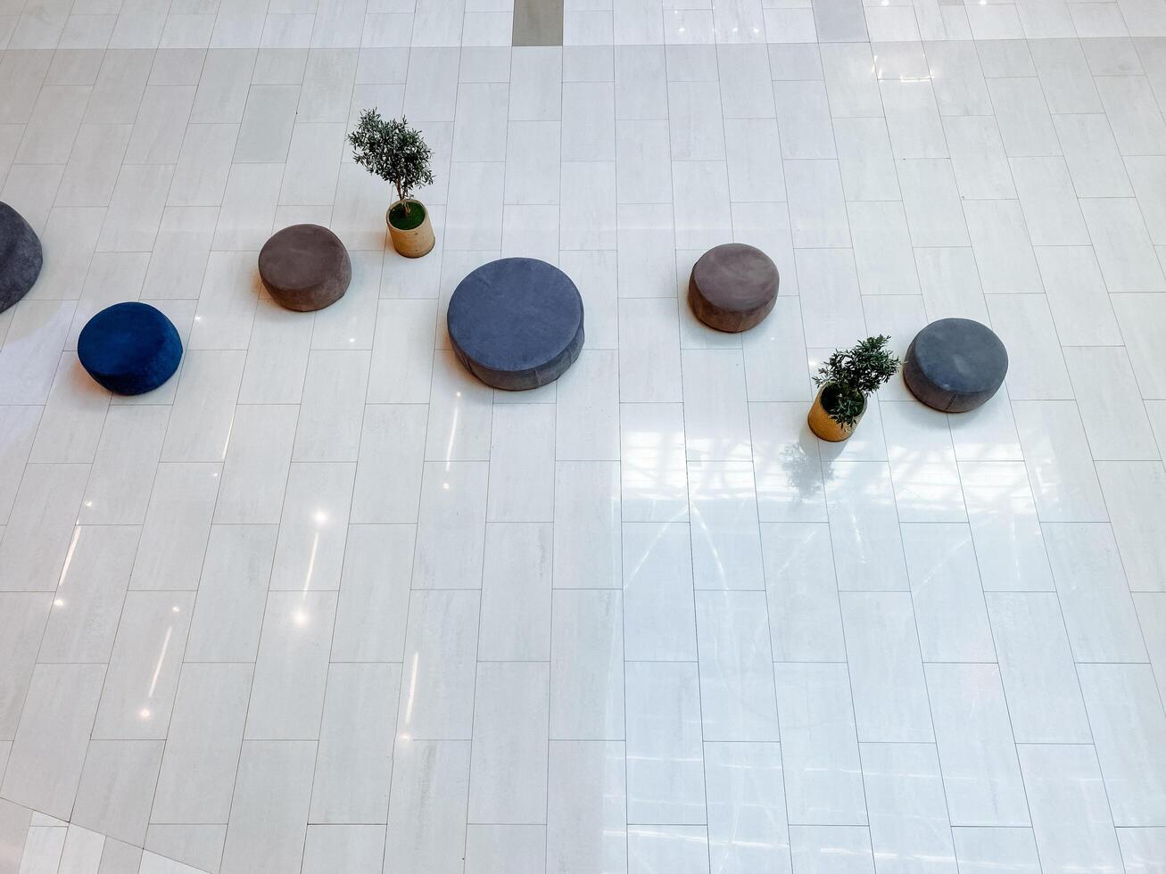 In a beautifully designed space, a group of comfortable ottomans and vibrant potted plants are arranged strategically on a stylish white tiled floor, creating an inviting atmosphere photo