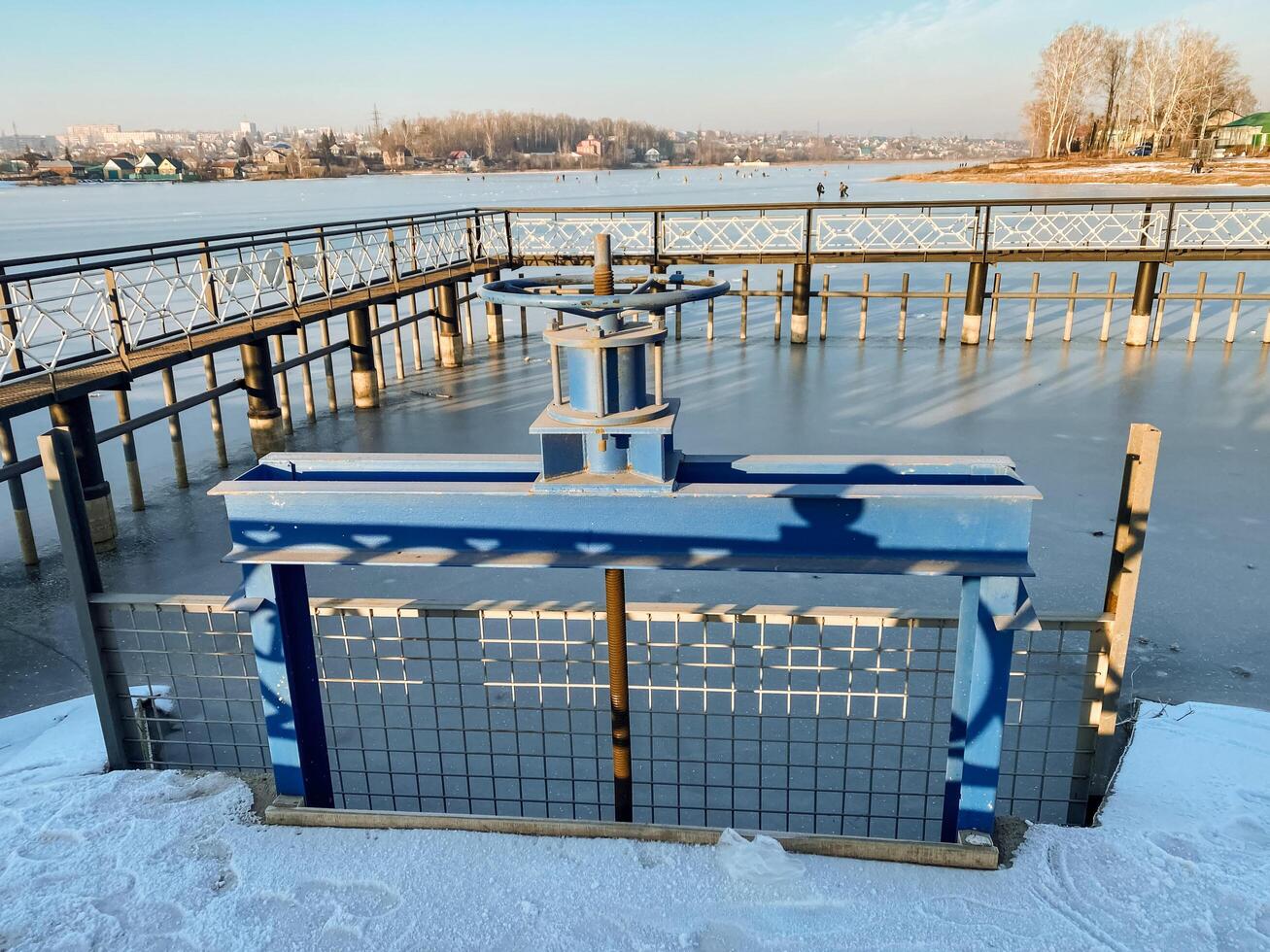 The image captures a serene frozen lake, where a rustic wooden fence stands out prominently in the foreground, beautifully enhancing the overall tranquility of this picturesque winter scene photo