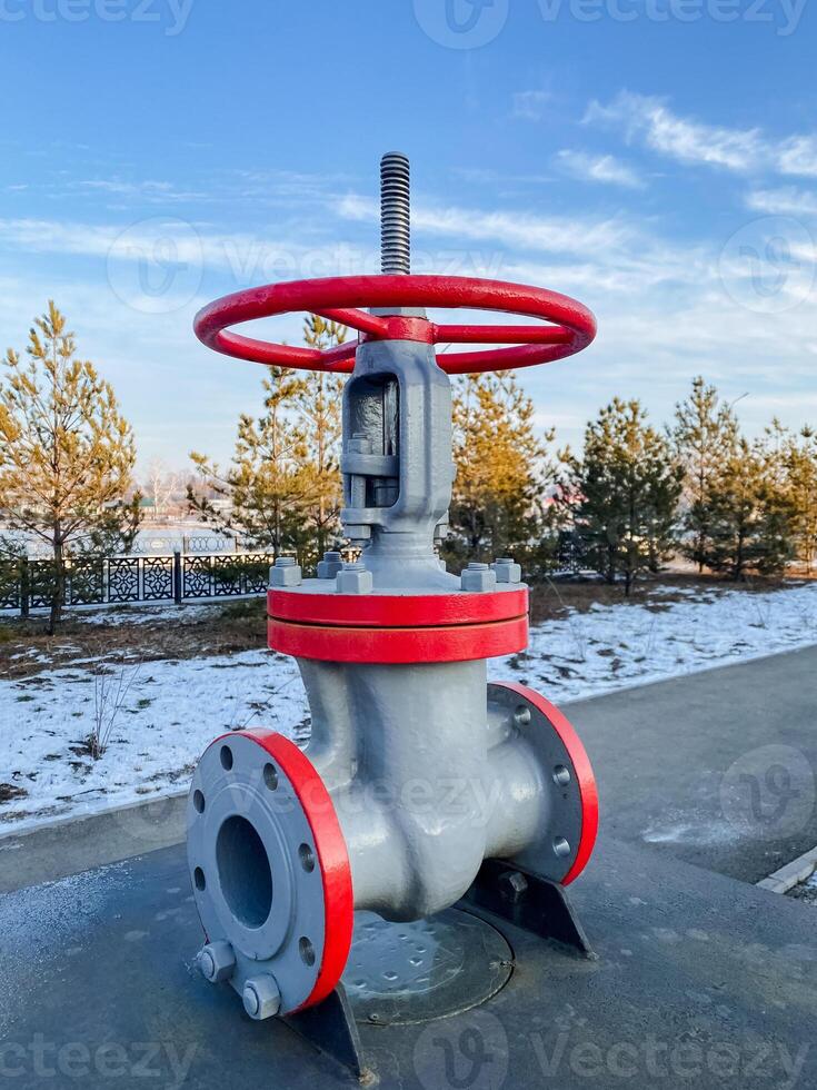 A bright redhandled valve is positioned on the side of the road, its vibrant color contrasting with the surrounding environment, including passing vehicles and road surfaces photo