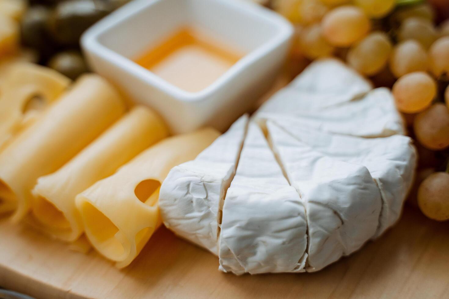 A beautifully crafted wooden cutting board is adorned with an assortment of gourmet cheese, fresh grapes, savory olives, and a drizzle of sweet honey, creating a delightful presentation photo