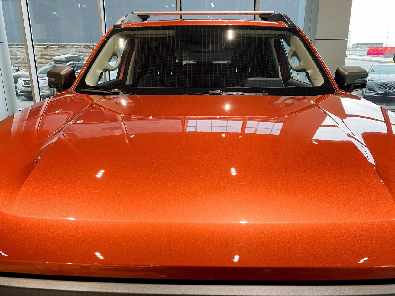 This image features a detailed closeup of an eyecatching orange car displayed within a modern showroom setting, showcasing its sleek design and vibrant color, drawing attention photo