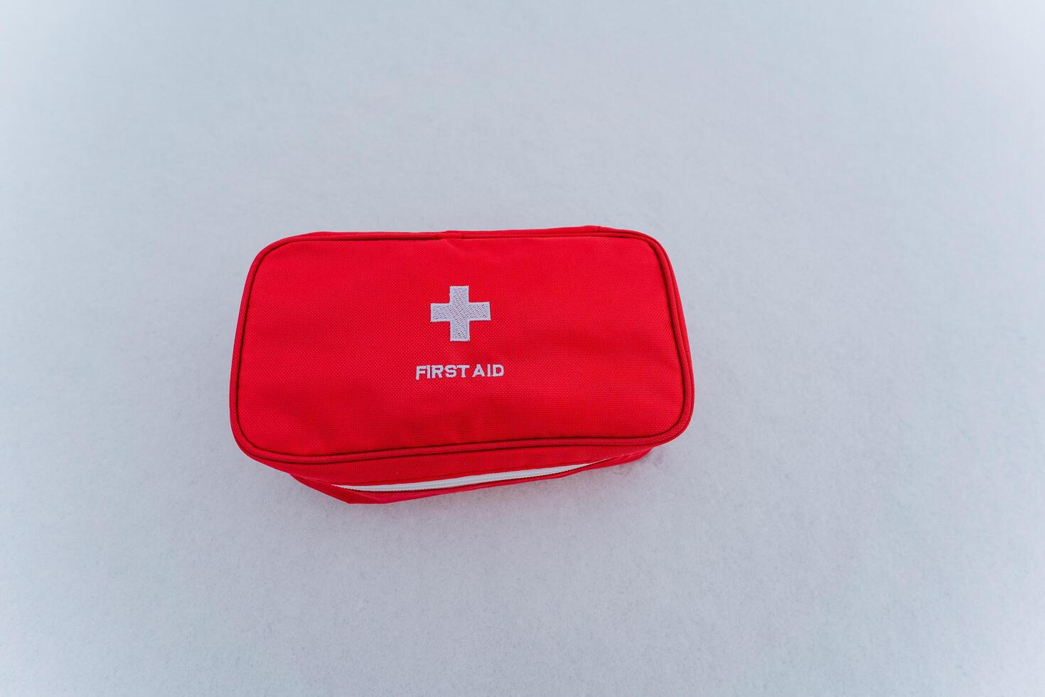 A bright red first aid kit featuring a prominent white cross emblem is placed carefully on a clean white surface, making it easily noticeable for health care and emergency medical needs photo