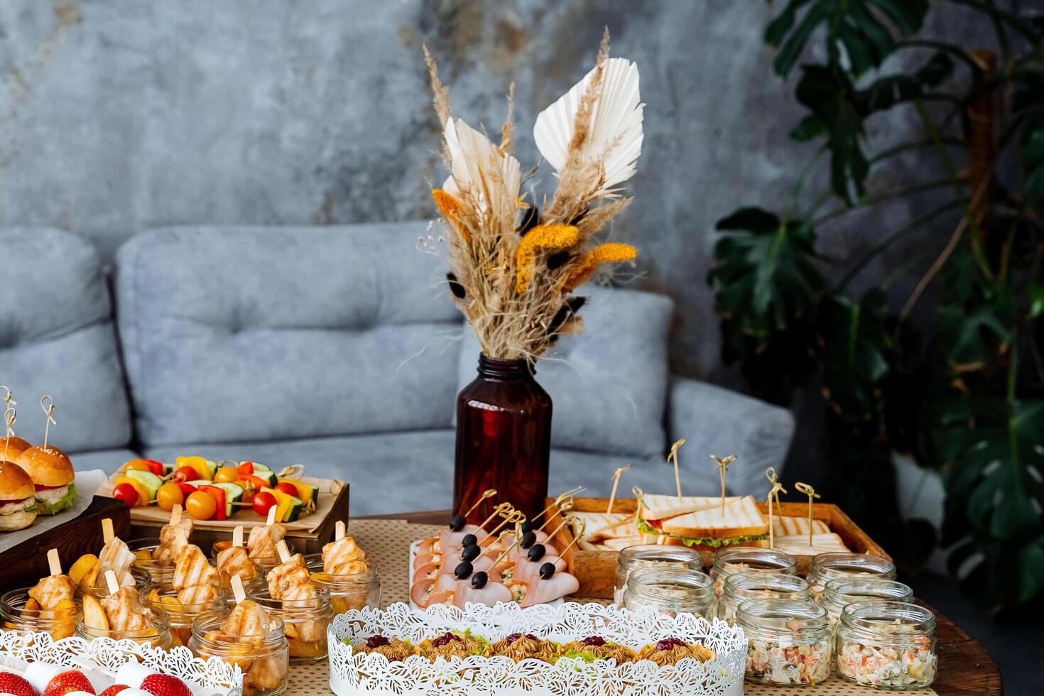 On the table, there is an elaborate spread filled with a wide variety of delicious food items, along with a beautiful vase that holds dried flowers, adding a charming touch to the setting photo