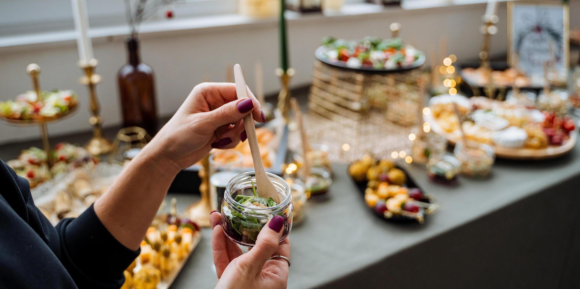 A woman proudly holds a shiny spoon in front of an exquisitely arranged buffet table, which is filled with an impressive array of various delicious foods and delightful treats of every kind photo
