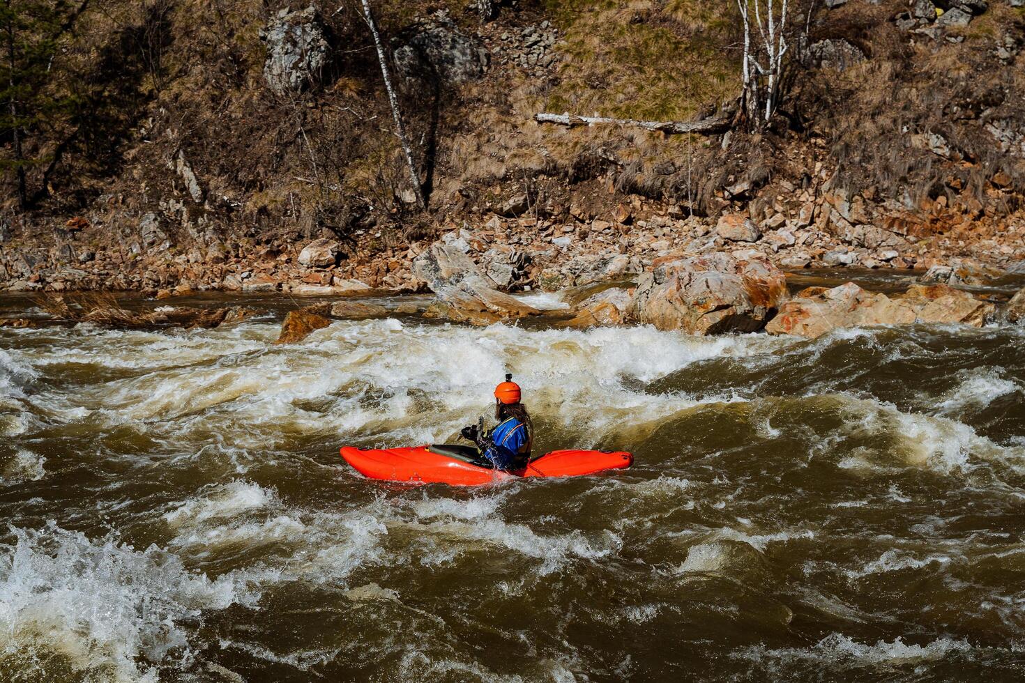 A person skillfully navigates a bright orange kayak on a rushing river, enjoying the thrilling adventure and stunning natural beauty, making the experience unforgettable photo