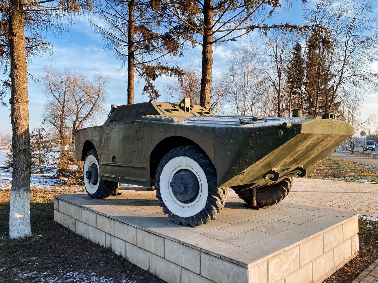 A military vehicle is currently positioned atop a concrete block, adding to the unique scenery of its surroundings, contrasting with the elements like clouds and trees in the backdrop photo