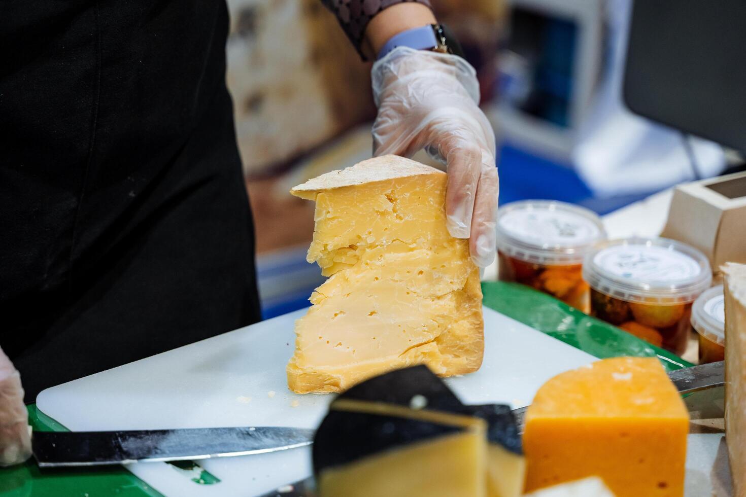 A person is actively engaged in the process of cutting a large piece of cheese on a wooden cutting board, which is a common practice in food preparation and cooking activities photo