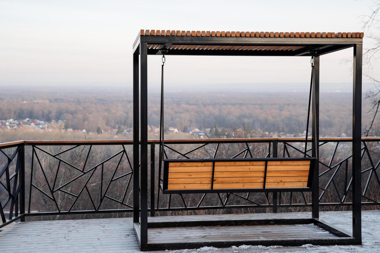 A beautiful wooden swing is positioned on a spacious balcony that provides a stunning view overlooking a lush forest, creating a perfect spot for relaxation and reflection photo