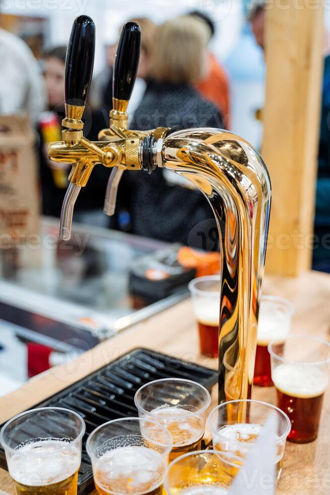 A shiny beer tap pours refreshing golden beer into cups on a polished wooden counter, creating a vibrant atmosphere for patrons to enjoy drinks with friends and fellow guests photo