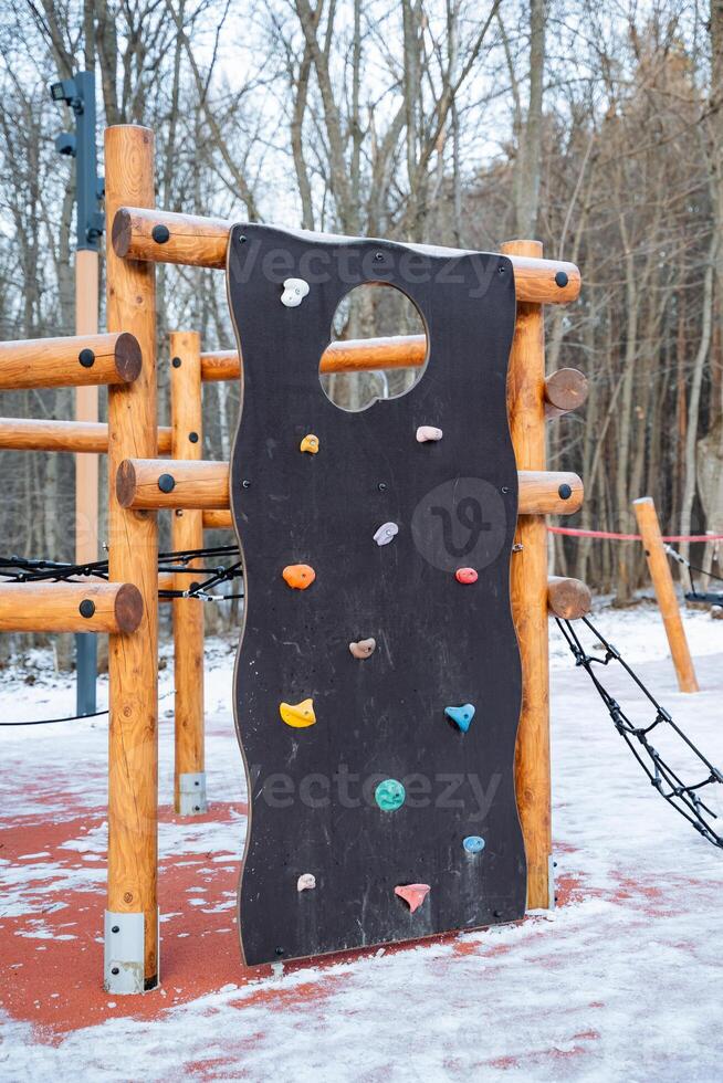 In a snowy playground, there stands a climbing wall featuring a unique hole right in the center, creating an exciting challenge for children and adding to the fun atmosphere of winter photo