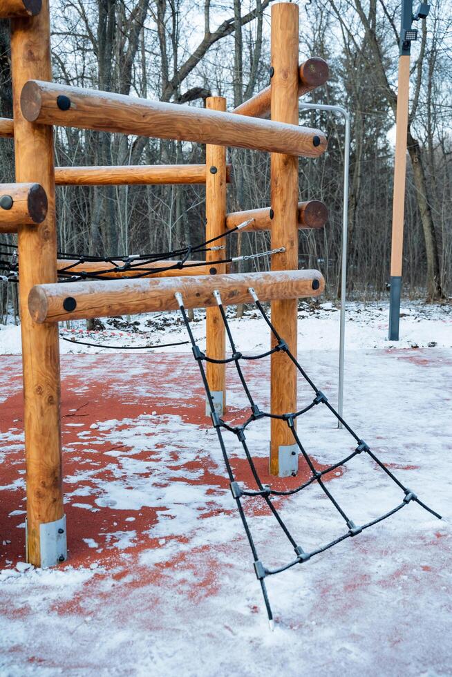 A beautifully crafted wooden playground adorned with a sturdy rope ladder surrounded by a blanket of fresh, white snow, offering a perfect spot for childrens play and recreation photo