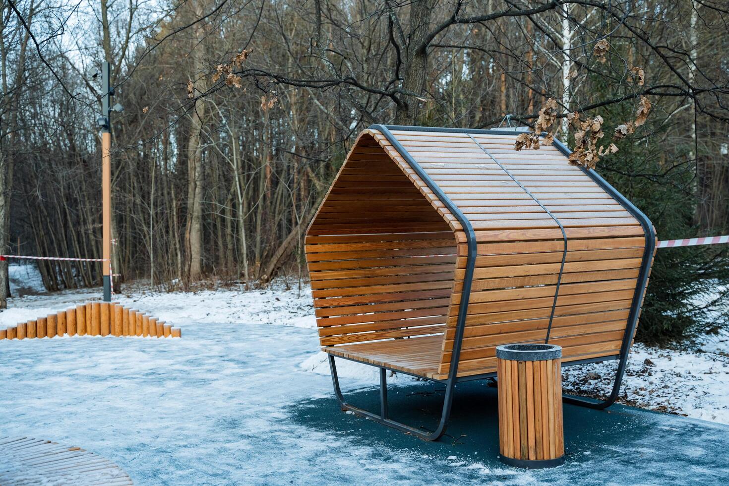 In a winter wonderland, a charming wooden bench sits beside a trash can in a snowy park, creating a picturesque scene amidst the serene beauty of nature and the falling snowflakes photo