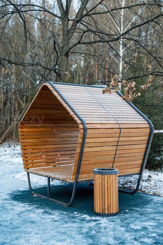 In a picturesque park, there is a charming wooden bench situated right next to a conveniently placed trash can, creating a comfortable and clean space for visitors to relax photo