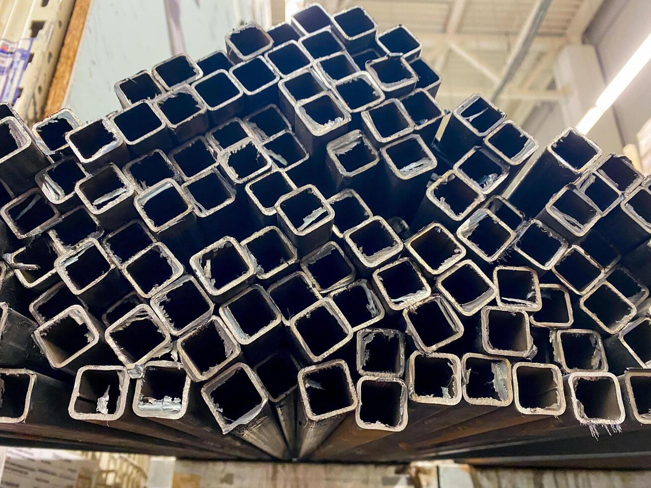 A significant number of squareshaped metal pipes are neatly arranged and stacked one on top of another, creating a tall structure or pile that showcases their uniform shape and size photo