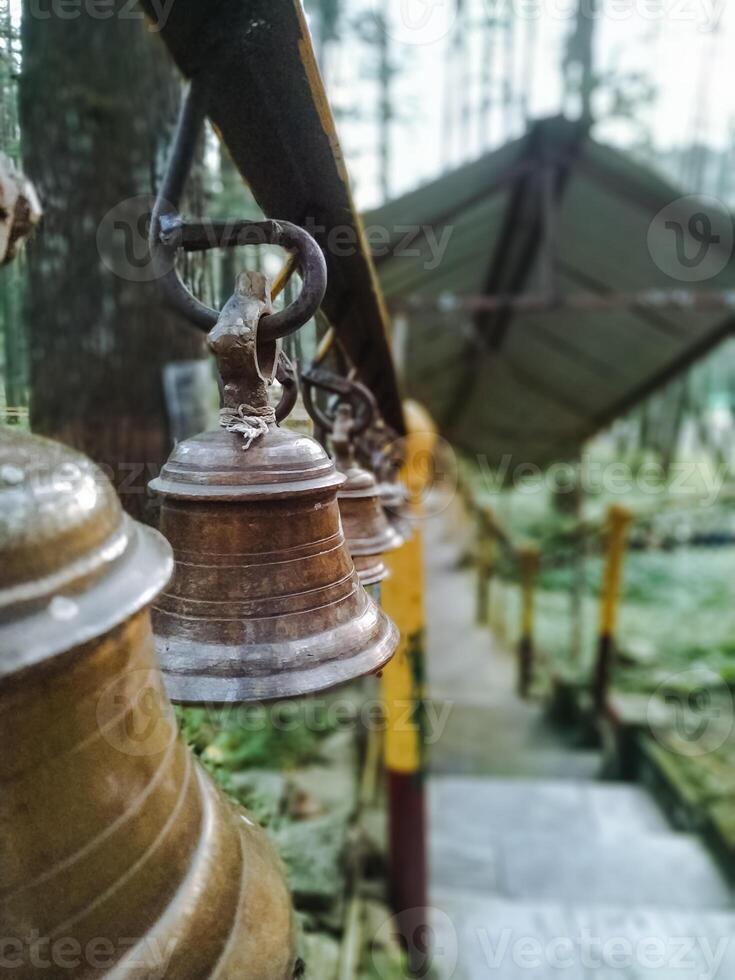 A row of bells hanging from a pole in a forest photo