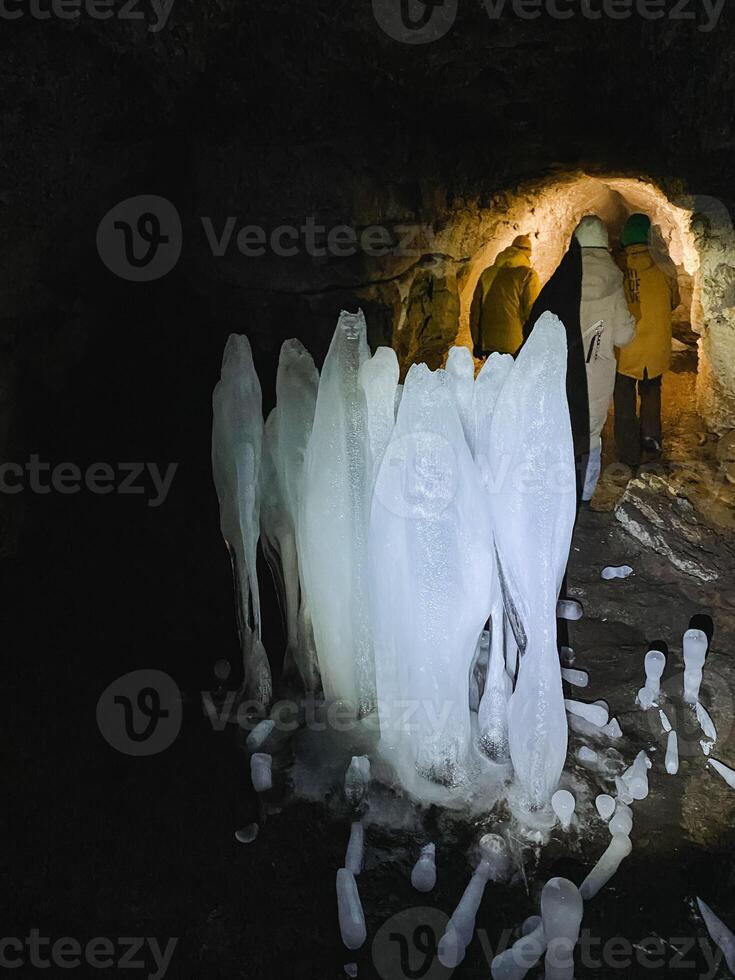 A person is carefully walking through a natural cave that features stunning and unique ice formations hanging from the ceiling and surrounding the paths, creating a breathtaking scene photo
