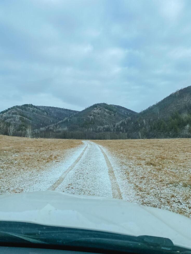 A car is navigating its way down a dusty dirt road, surrounded by majestic mountains rising prominently in the background, creating a picturesque landscape filled with natural beauty photo